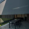 Een modern terras met een gedeeltelijk neergelaten grijs uitschuifbaar scherm dat een eettafel met zes stoelen beschaduwt. Potplanten staan op de tafel en in de hoek; buiten is groen gras zichtbaar.