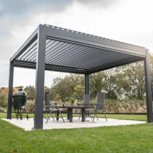 Een moderne buitenprieel met een strak metalen frame staat op een terras. Daaronder staat een eettafel met stoelen en decoratieve planten. Rondom het prieel ligt een goed onderhouden gazon en bomen op de achtergrond onder een bewolkte lucht.