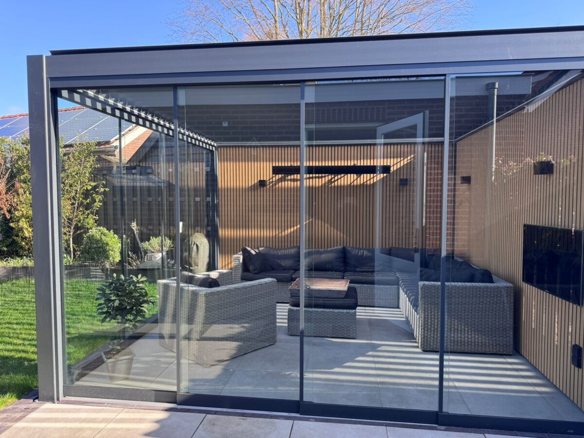 Een luxe lamellen overkapping met glazen schuifwanden vormt hier een stijlvolle en functionele buitenruimte. De kantelbare lamellen in het dak zorgen voor optimale licht- en schaduwregeling, terwijl de glazen wanden beschutting bieden tegen de wind en regen.