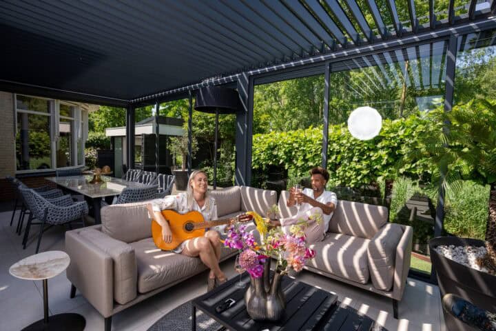 Benadrukt de stijlvolle lamellenoverkapping en gezellige zithoek met twee mensen, muzikant en drinkend, in tuin.