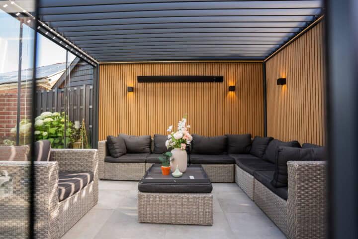 Luxe buiten lounge met houten wand en comfortabele wicker bank met zwarte kussens.